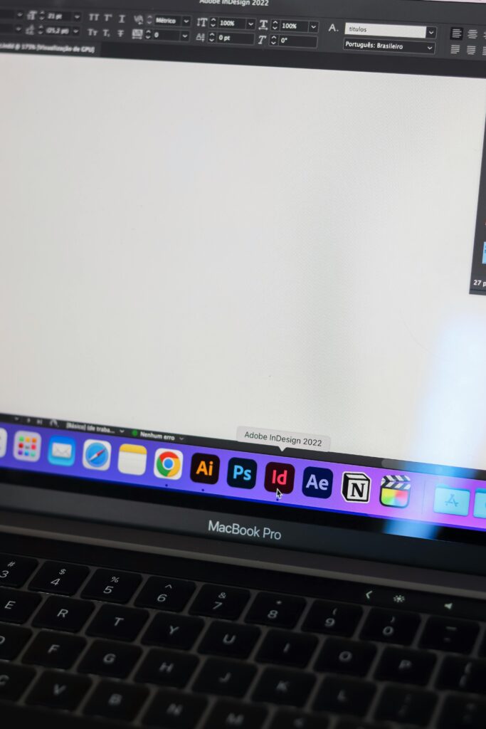 A detailed view of a MacBook Pro displaying Adobe InDesign and other design tools on screen.