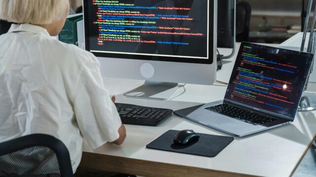 Woman programmer coding on dual monitors in a modern office setting, focusing on software development.