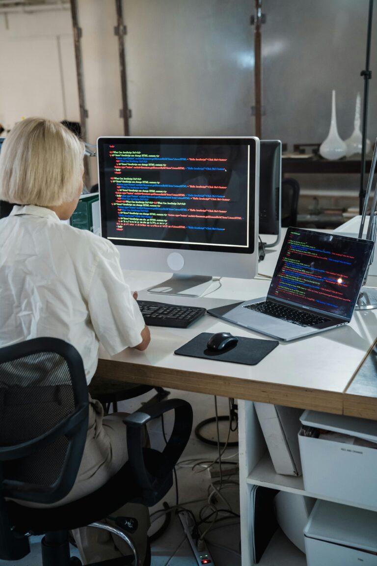 Woman programmer coding on dual monitors in a modern office setting, focusing on software development.