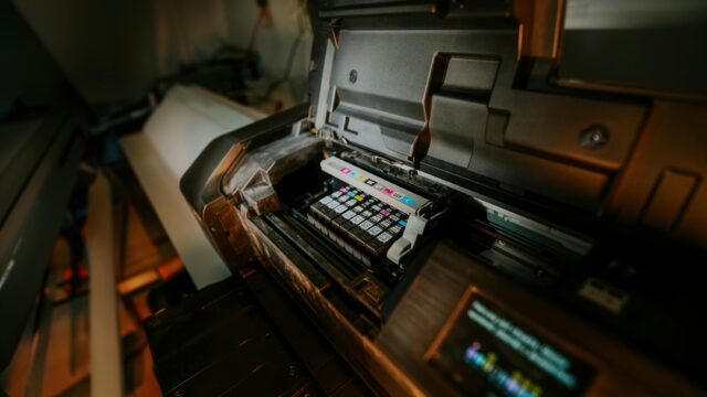 Close-up view of an inkjet printer with exposed cartridges in a workspace setting.