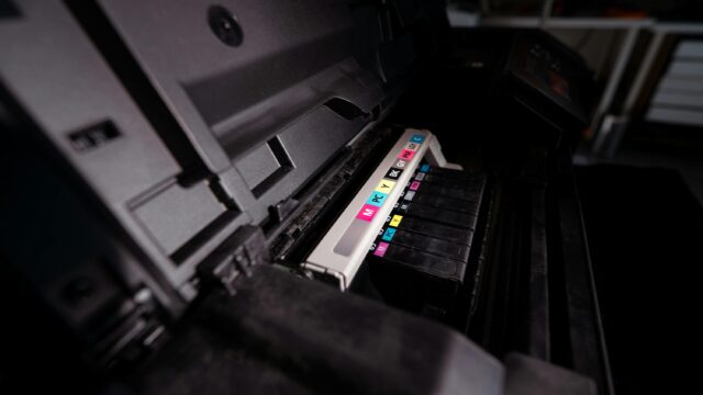 Detailed view of open printer with visible CMYK ink cartridges in a dark setting.