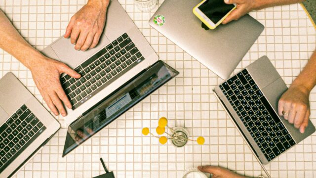 Top view of a team collaborating with laptops, phones, and notes in a modern office.