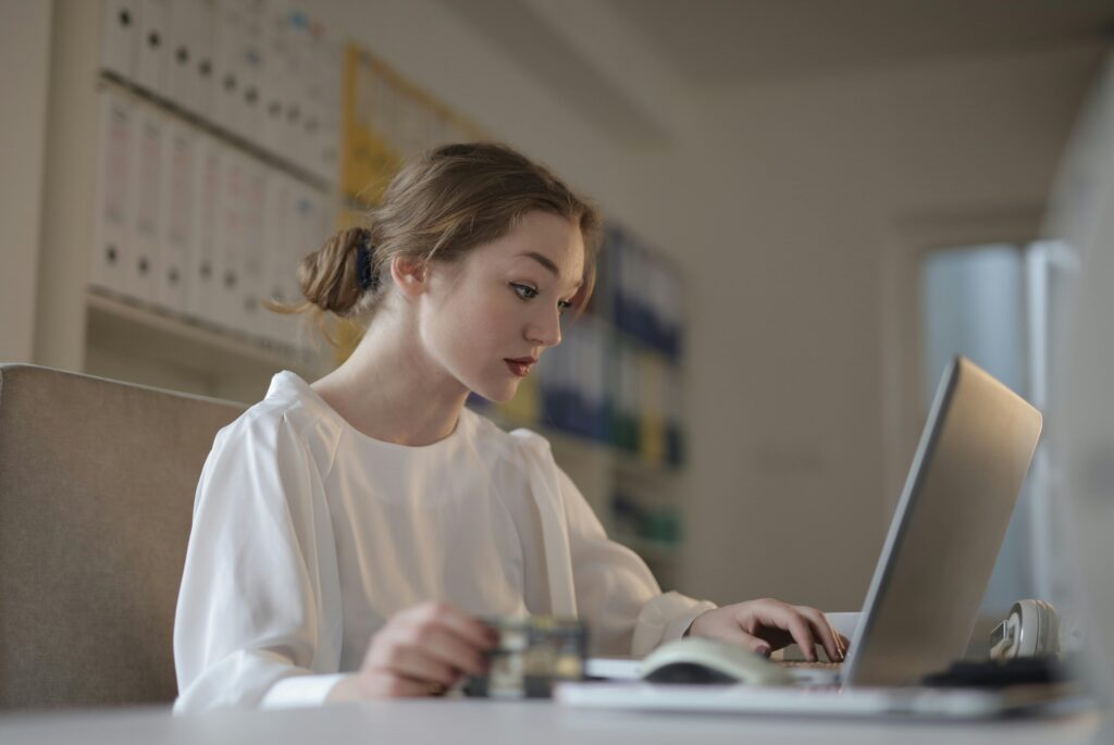 Focused young woman working remotely on a laptop in a modern office.