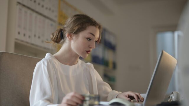 Focused young woman working remotely on a laptop in a modern office.