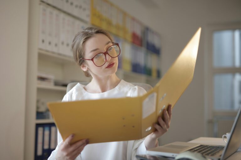 Caucasian woman intensely reading documents in an office setting.