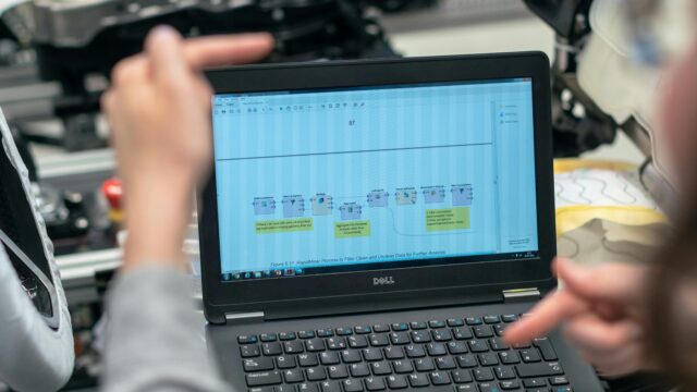 Engineers using a laptop to analyze software data in an industrial workshop setting.