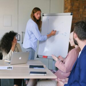 Pensive employee in formal clothes drawing graph on flipchart while explaining project to coworkers during seminar in workspace in daytime