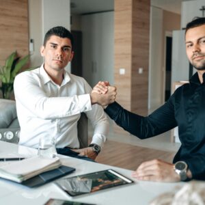 Two businessmen in an office engaging in a handshake, representing partnership and agreement.