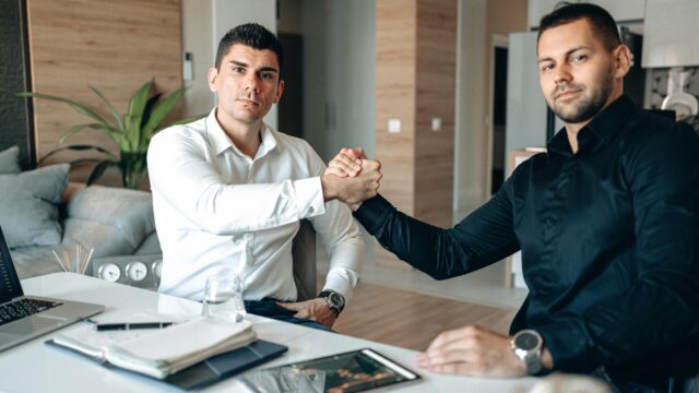Two businessmen in an office engaging in a handshake, representing partnership and agreement.