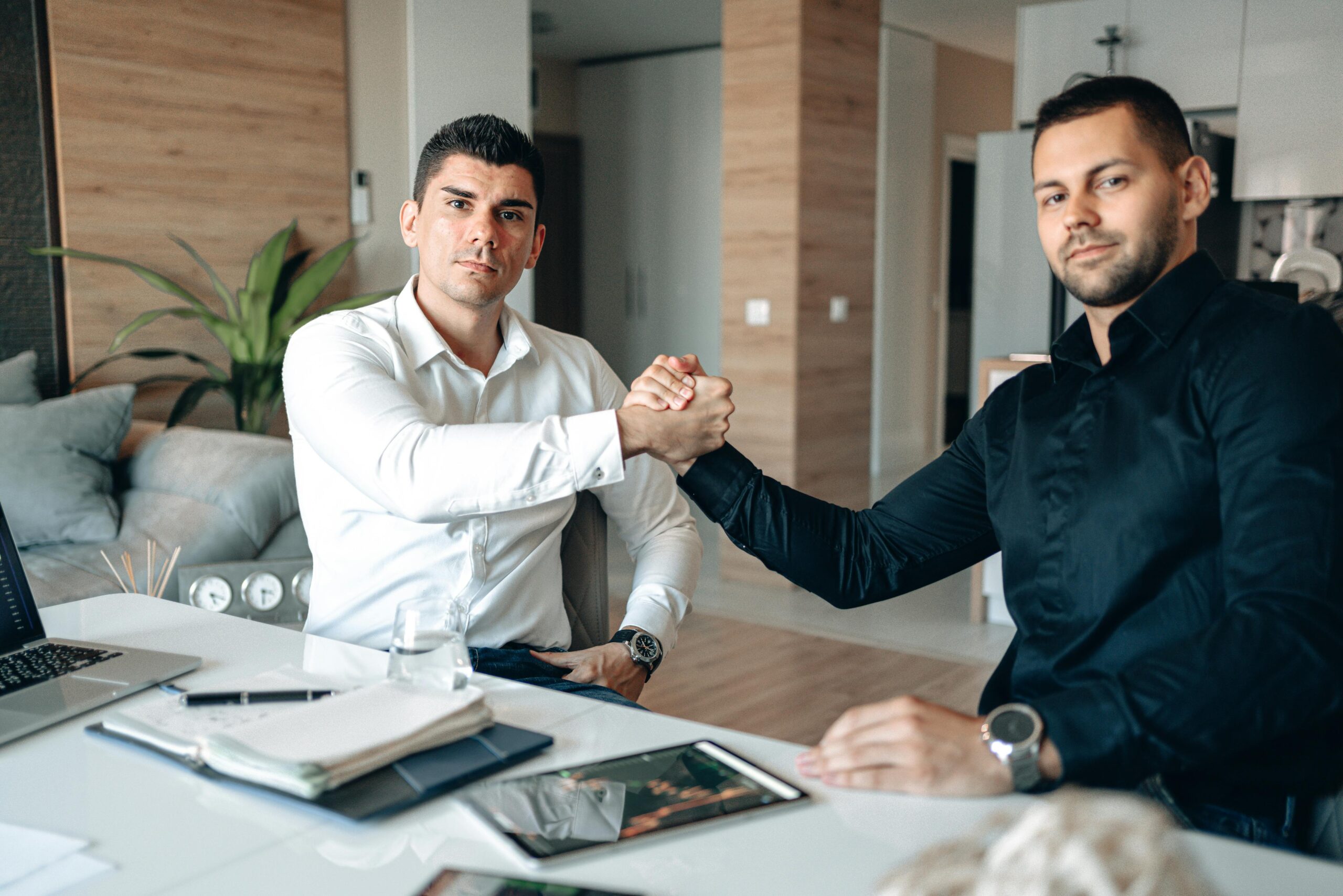 Two businessmen in an office engaging in a handshake, representing partnership and agreement.