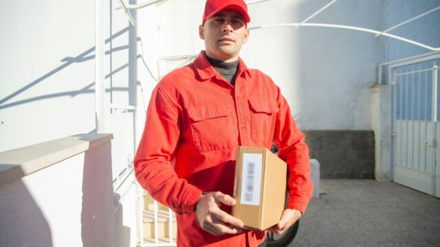A male delivery worker in a red uniform holding a package outdoors in Portugal.