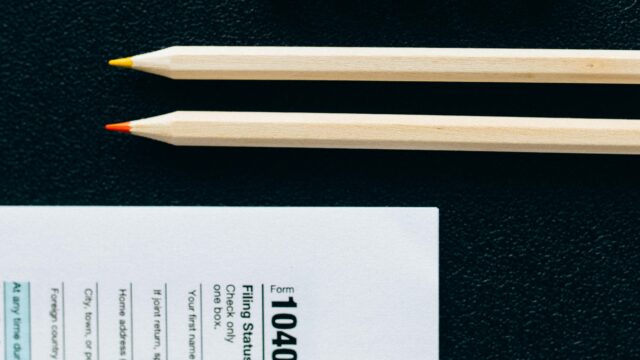 Wooden pencils and 1040 tax form on black background with tiles spelling 'TAXES'.