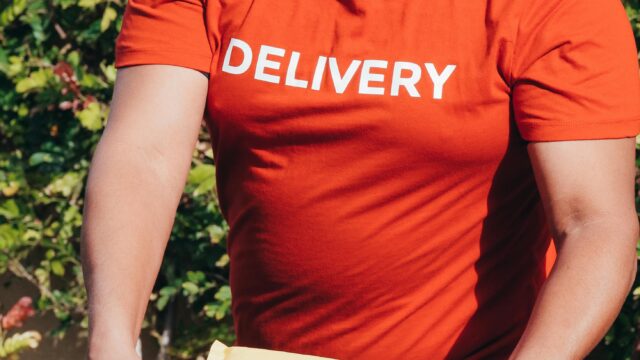 A delivery man in a red shirt holding packages, delivering service outdoors.