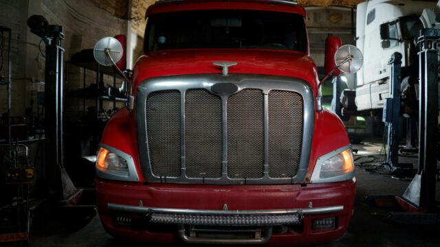 Front view of a red truck parked in a dimly lit industrial garage setting.