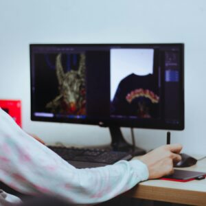 A digital artist editing designs on a computer with a stylus in an indoor workspace.