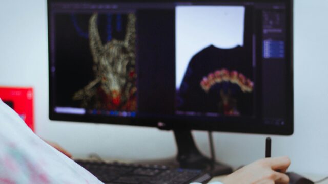 A digital artist editing designs on a computer with a stylus in an indoor workspace.