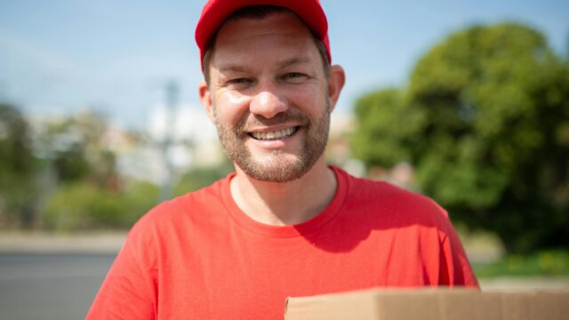 Happy deliveryman holding a box outdoors in Portugal, showcasing delivery service.