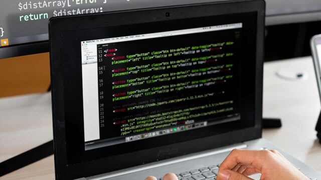 Person coding at a desk with laptop and external monitor showing programming code.
