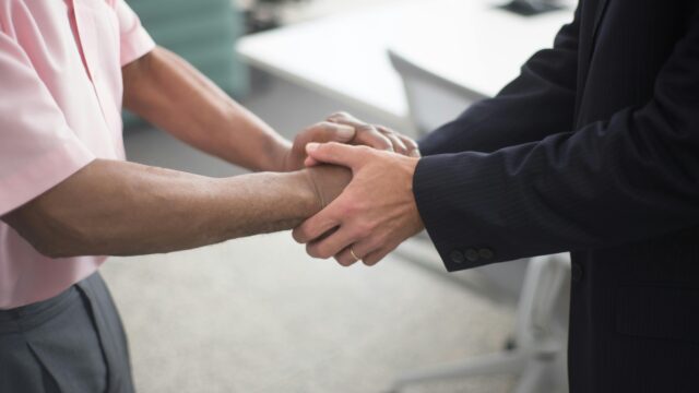 Close-up of a formal handshake between two businessmen in an office environment.