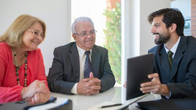 Elderly couple discussing real estate options with an agent in a modern office setting.