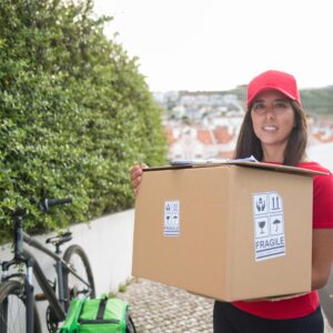 A delivery woman in Portugal carries a package with a bicycle in the background, showcasing urban parcel delivery.